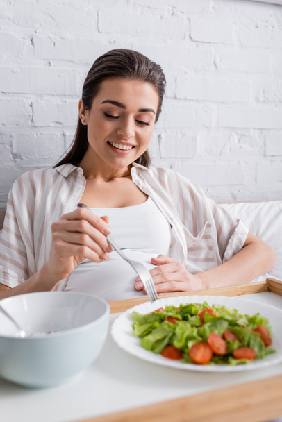 cheerful pregnant woman holding fork near tasty meal on tray - Photo, Image