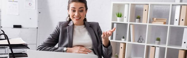 cheerful pregnant businesswoman gesturing near laptop in office, banner - Foto, immagini