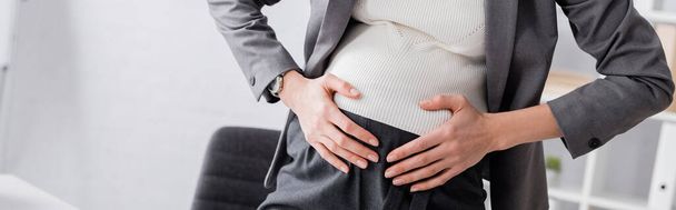 cropped view of young pregnant businesswoman touching belly while feeling cramp, banner - Фото, изображение