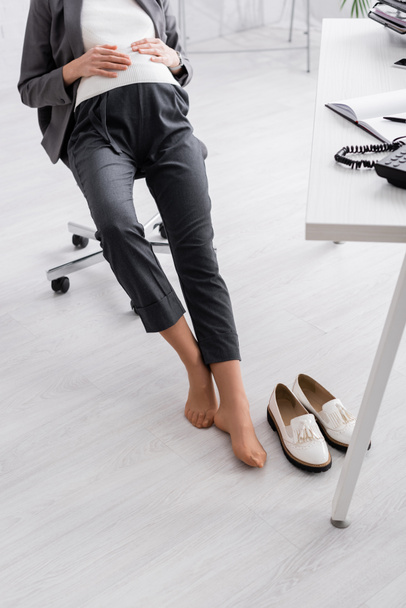 Ofiste sandalyede oturan ayakkabısız hamile kadın manzarası. - Fotoğraf, Görsel