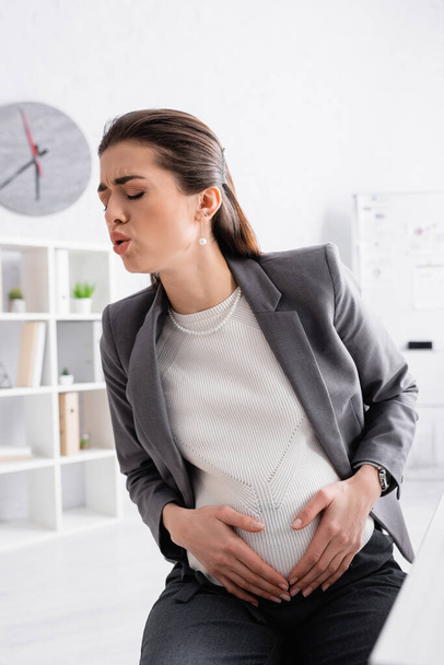 pregnant businesswoman touching belly while feeling cramp  - 写真・画像