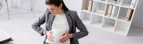 high angle view of displeased pregnant businesswoman touching belly while feeling cramp, banner - Photo, image