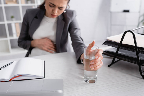 blurred pregnant businesswoman feeling cramp and reaching glass of water  - Foto, Bild
