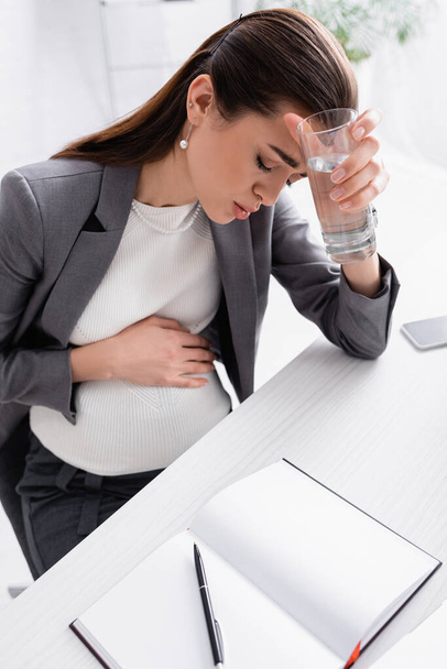 Empresaria embarazada sosteniendo un vaso de agua mientras se siente mal  - Foto, imagen