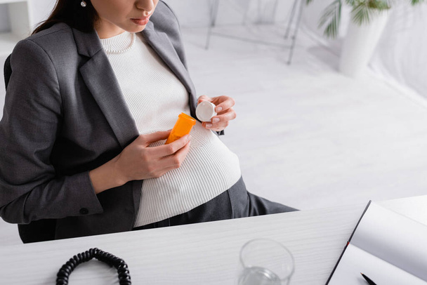 levágott kilátás terhes nő gazdaság üveg tabletták az irodában - Fotó, kép