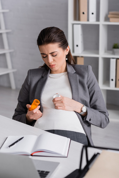 беременная женщина держит банку с таблетками в офисе - Фото, изображение