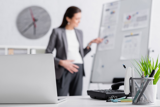 laptop near pregnant businesswoman near flip chart on blurred background  - Foto, afbeelding