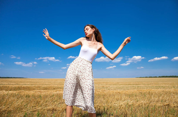 Young beautiful girl in the background of mown wheat field and blue sky - Fotografie, Obrázek