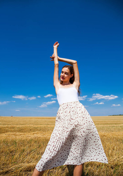 Young beautiful girl in the background of mown wheat field and blue sky - Φωτογραφία, εικόνα