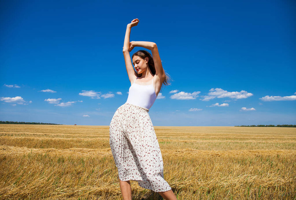 Young beautiful girl in the background of mown wheat field and blue sky - Foto, afbeelding