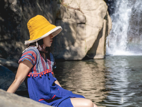 Women wear traditional Thai costumes and yellow hats. Sitting by the waterfall - Foto, afbeelding