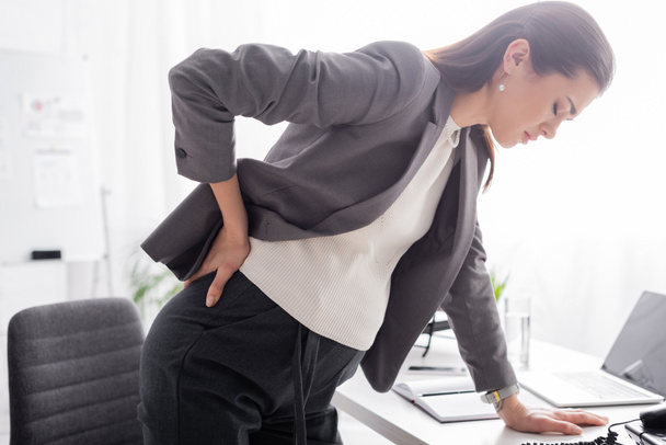 pregnant businesswoman suffering from pain and leaning on desk in office - Fotoğraf, Görsel
