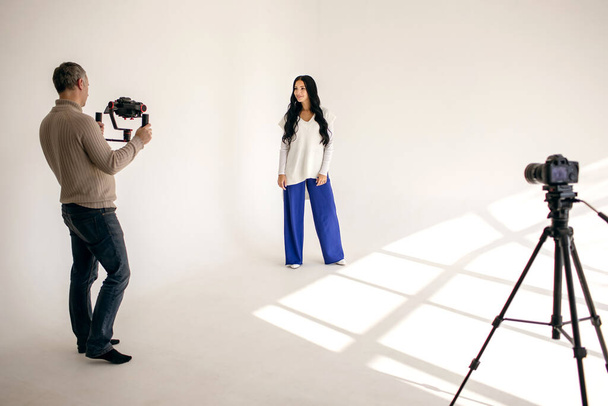 Egy női blogger videóblogot készít egy stúdióban egy videós segítségével, két professzionális videokamerával. Modern munka bloggerként vagy újságíróként az előfizetők számára - Fotó, kép
