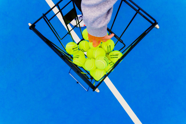 バレンシア,スペイン- 2021年4月26日:テニスプレーヤーは練習中にバスケットからダンロップテニスボールを拾う. - 写真・画像