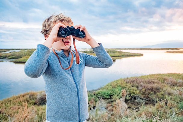 Un chico aventurero explora el paisaje con prismáticos con el horizonte nublado, concepto de crecer con independencia y futuro. - Foto, imagen