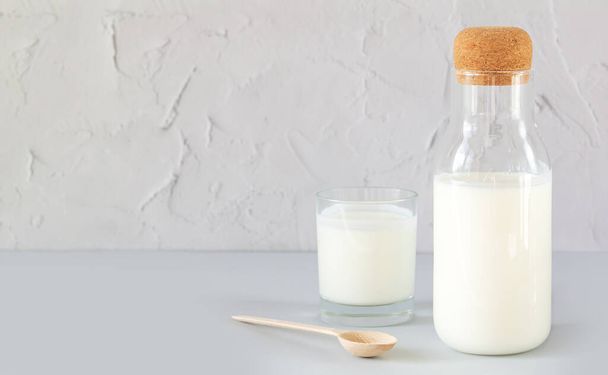 Tarro vintage con corcho de yogur casero, kéfir, leche fermentada o crema agria junto a vaso de beber y cuchara de madera en la mesa de la cocina - Foto, imagen
