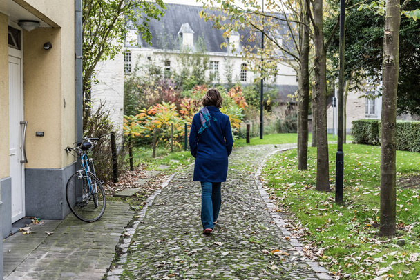 Thirty year old woman walking away on a cobble stone path in the medieval city center of Oudenaarde, Flanders, Belgium, Oct. 2017 - Zdjęcie, obraz