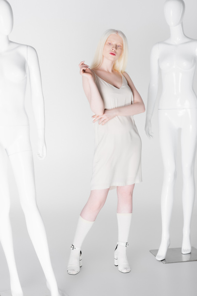 Mujer albina con estilo posando cerca de maniquíes sobre fondo blanco  - Foto, imagen
