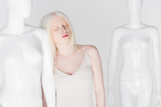 Молода альбіносова жінка з закритими очима, що стоїть поруч з манекеном ізольована на білому
  - Фото, зображення