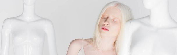 Albino-Frau mit geschlossenen Augen steht neben Schaufensterpuppe isoliert auf weißem Banner  - Foto, Bild