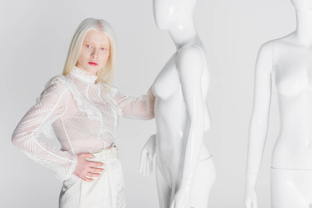 Stylish blonde woman holding hand on hip near mannequins isolated on white  - Foto, Imagem