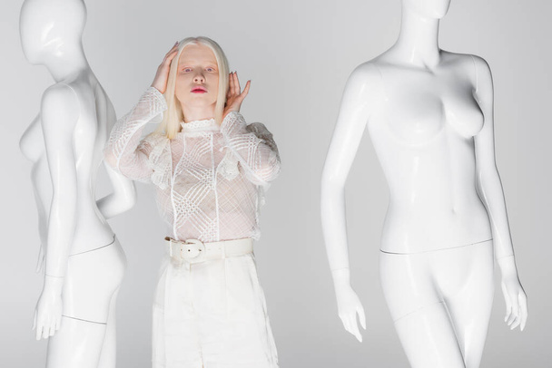 Stylowa kobieta albinos patrząc na kamerę w pobliżu manekinów izolowanych na szarości - Zdjęcie, obraz