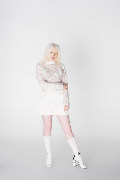 Pretty albino woman in sandals and blouse looking at camera on white background  - Fotó, kép