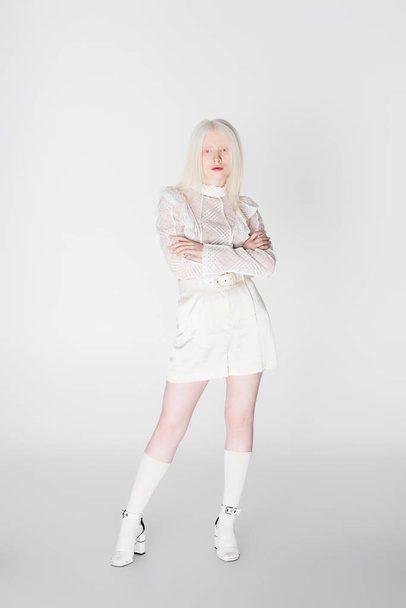 Longitud completa de elegante mujer albina y rubia con brazos cruzados sobre fondo blanco  - Foto, imagen