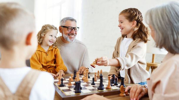 Crianças irmão e irmã jogando xadrez enquanto sentado na sala de estar com avós seniores - Foto, Imagem