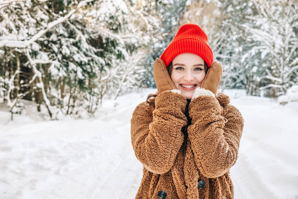 Skin protection in winter frosty time concept. A young attractive woman holding frozen cheeks in a winter park.  - Photo, image