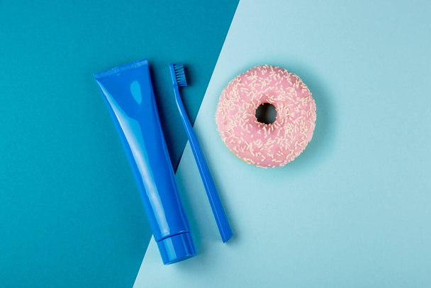 Blue tube of toothpaste blue toothbrush and pink donut lie on combined blue background. Top view - Foto, Imagem
