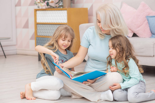 Caucasian mom reading a book to children sitting on the floor in the living room. Happy family concept. - 写真・画像
