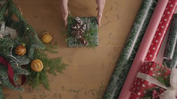 Ein Top-Down-Plan. Voll sichtbar der Tisch mit den Dekorationen. Weihnachtsgeschenk in Bastelpapier verpackt auf einem Holztisch. Bandage und gebundene Schleife. - Filmmaterial, Video