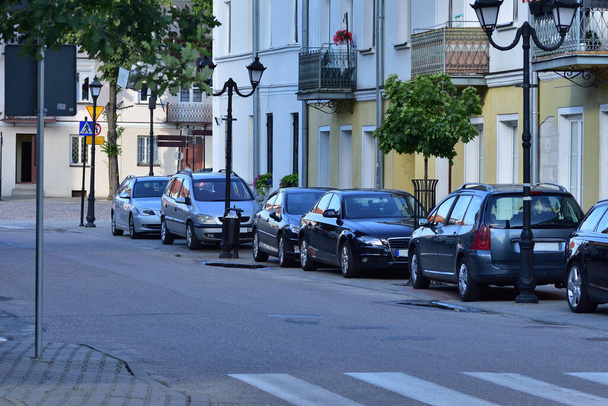 Osobní automobily stojící na parkovišti odděleném od veřejné komunikace vedle obytných domů.  - Fotografie, Obrázek