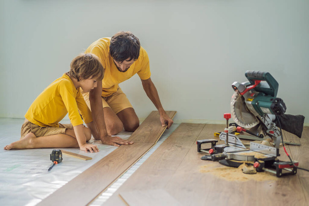 Father and son installing new wooden laminate flooring on a warm film floor. Infrared floor heating system under laminate floor - Foto, Bild