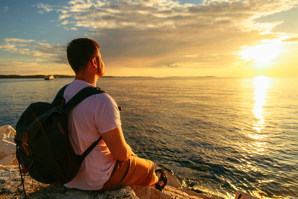 man with backpack enjoying sunset over the sea. copy space. summer vacation - Фото, изображение