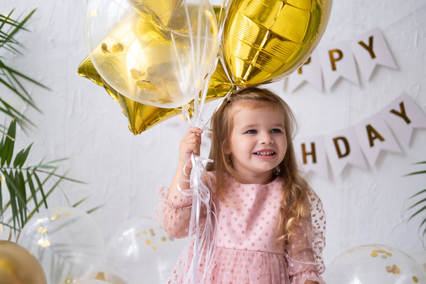 šťastná malá blondýnka v růžových šatech drží balónky a slaví své narozeniny - Fotografie, Obrázek
