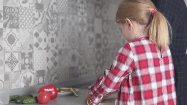 小さな女の子と彼女の母親は台所で家で魚や野菜とピタパンを調理します - 映像、動画