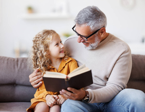 Schattig klein meisje kleindochter lezen boek met positieve senior grootvader - Foto, afbeelding