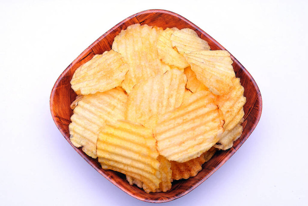 Patatas fritas acanaladas y crujientes en un tazón sobre un fondo blanco - Foto, Imagen