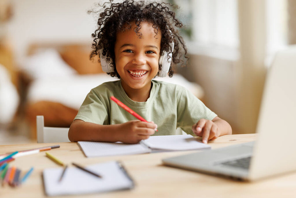 笑顔アフリカ系アメリカ人の子供の学校の男の子のヘッドフォンでオンラインで勉強ノートパソコンで自宅 - 写真・画像