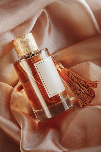 Perfume bottle on Golden silk folded fabric background. Glass flask with bronze liquid. - Foto, Imagem