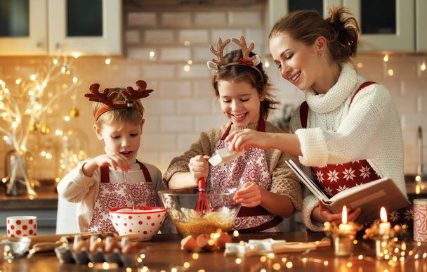 Молодая улыбающаяся женщина мама делает тесто для рождественского пряника печенье с милыми маленькими детьми - Фото, изображение