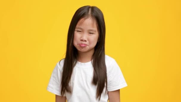 Tuhma pieni japanilainen tyttö murjottaa ja irvistää yli keltainen tausta - Materiaali, video