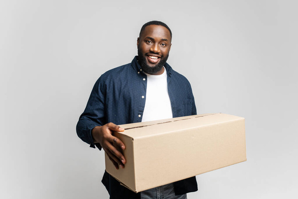 Glad young African-American man holding cardboard box, smiling and looking at camera - Foto, Bild