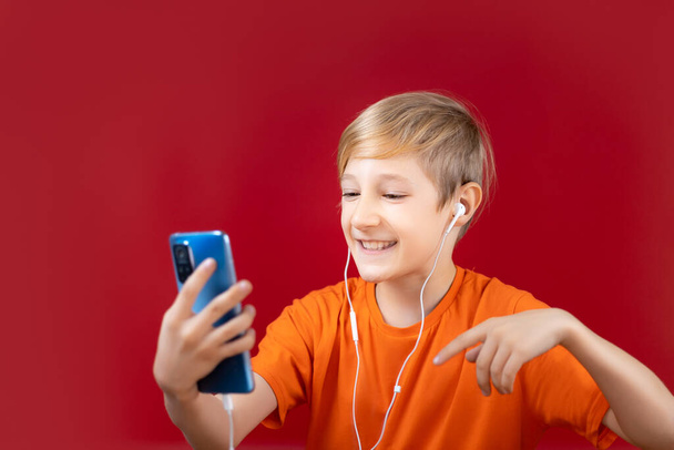 cheerful boy on a red background, holds a phone in his hand and emotionally gestures - 写真・画像