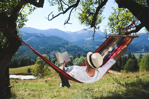 Человек читает книгу в гамаке на открытом воздухе в солнечный день - Фото, изображение