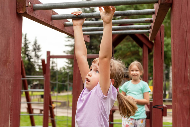 Elementary school age child exercising, climbing, playing on the playground, portrait, closeup. Children and healthy physical exercise and leisure activity outdoors simple concept, summer vacations - Photo, Image