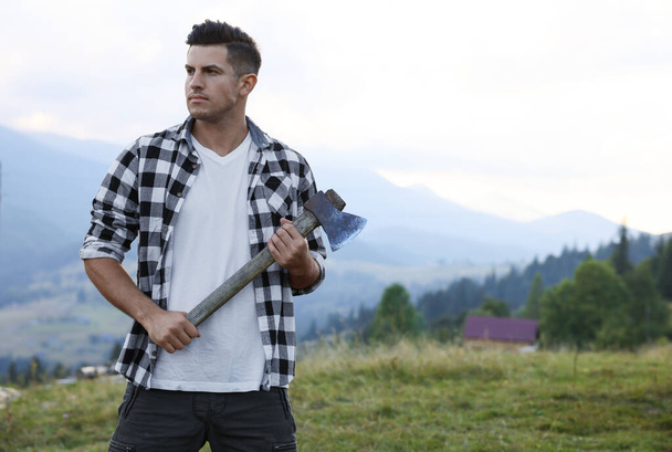 Handsome man with axe in mountains, space for text - Foto, immagini