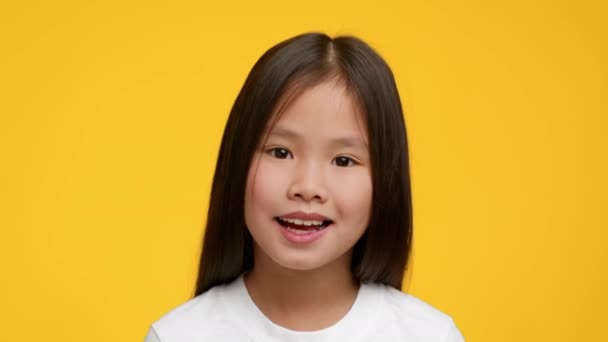 Retrato de adorable asiática preescolar chica posando sobre amarillo fondo - Imágenes, Vídeo